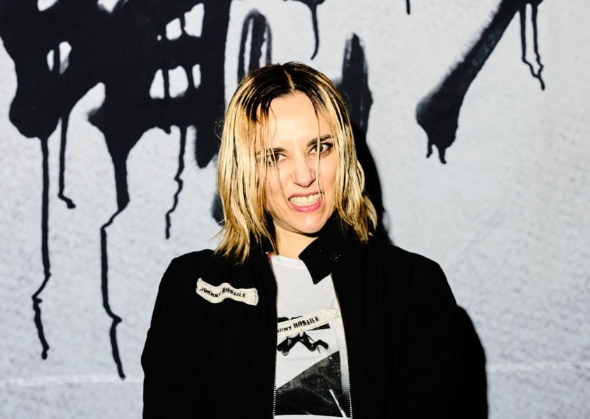 Jehnny Beth smiling infront of graffiti wallx